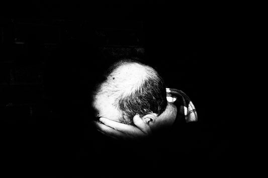 balding man in the dark with his face in his palm